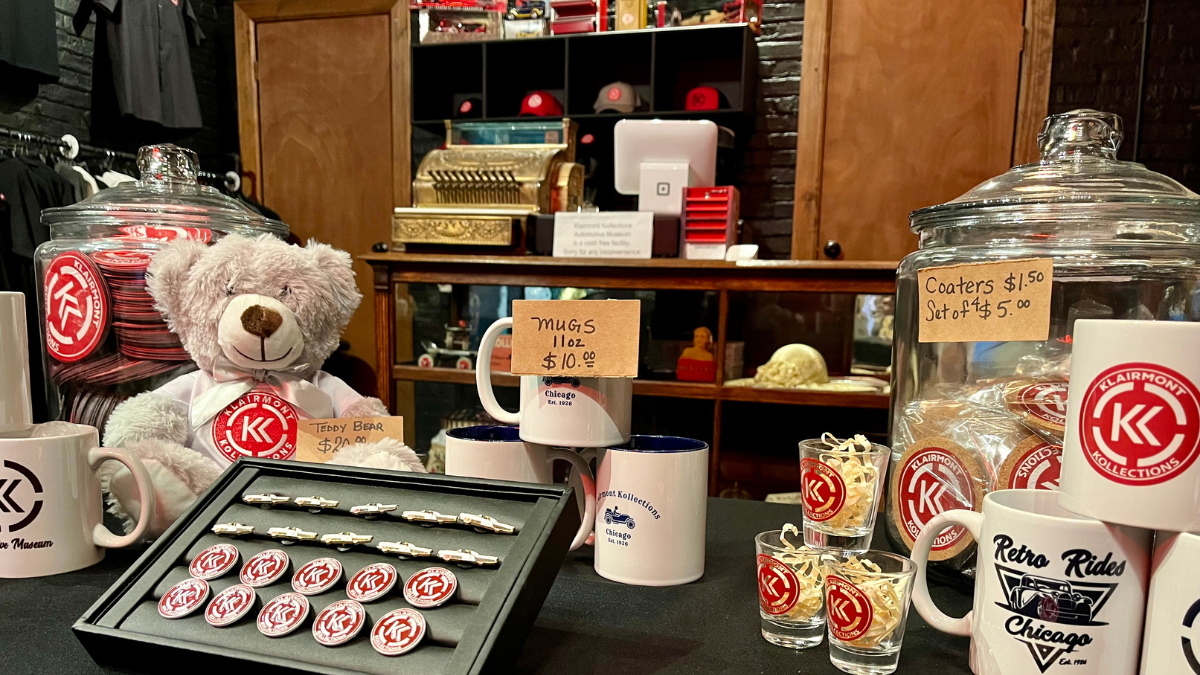 Photograph of our in-person gift shop, featuring our mugs, pins, and a teddy bear bearing the Klairmont Kollections logo.